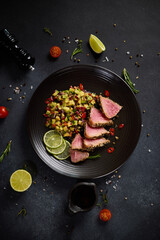 Sliced Organic grilled Tuna fillet covered with sesame seeds and salsa on black ceramic plate