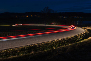 Light trails from car riding in curve asphalt street to small village at night. Transportation background, long exposure