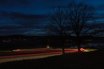 Light trails from car riding in curve asphalt street to small village at night. Transportation background, long exposure