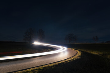 Light trails from car riding in curve asphalt street at night. Transportation background, long exposure