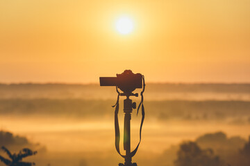 A professional photographer's camera on a tripod looks at the sunrise. Countryside landscape with...