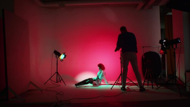 Photographer at work with model in studio against red backdrop. Behind the scenes of a photo shoot. Photography studio setup concept. Design for educational content, workshops, and studio brochure