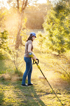 Teen girl cutting grass with whipper snipper in golden afternoon light