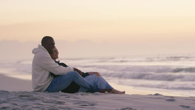 Shot of casually dressed loving young couple sitting on sand watching beautiful sunrise morning over beach and sea in South Africa - shot in slow motion