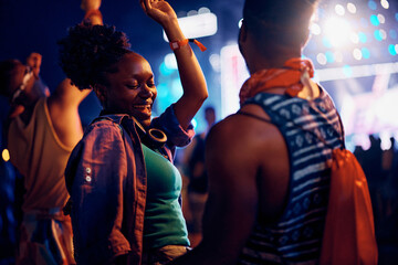 Happy black woman dancing with her boyfriend during open air music concert at night. - obrazy, fototapety, plakaty