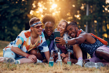 Carefree friends having fun and taking selfie while waiting for summer music concert in park.