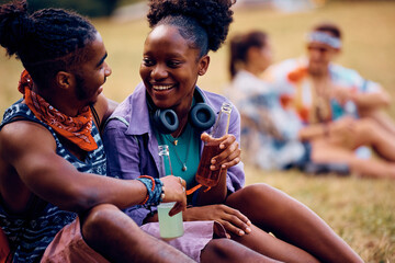 Happy black woman and her boyfriend having drink and talking during summer music festival.