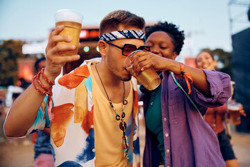 Young man drinking girlfriend's beer on music concert in summer.