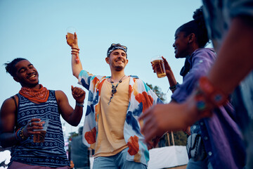 Cheerful man drinking beer and dancing with friend on music concert in summer.