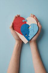 Adult and child hands holding heart puzzle on light blue background