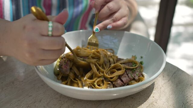Close up Hand of Woman Eating Beef stroganoff with herb pasta in Restaurant at daytime. concept of food 