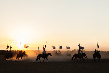 Shadows and silhouettes of horses and riders with australian flags on dust at sunset