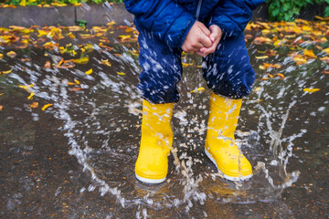 Kid jumping in the puddle. Rubber waterproof yellow boots.