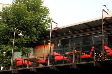 Bright red chairs and tables on large outdoor balcony of second floor wood house with glass fence.