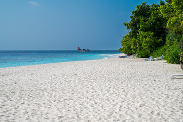 Beautiful sandy beach with a dense green forest. Seaplane floats on the sea.