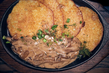 Potato pancakes with mushrooms in sauce in a cast iron frying pan on a wooden tray..Serving a simple dish