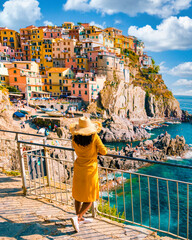 Asian women visiting Manarola in Cinque Terre Italy,beautiful colorful town of La Spezia Liguria one of the five Cinque Terre, woman with hat standing by the ocean during summer in Europe © Fokke Baarssen