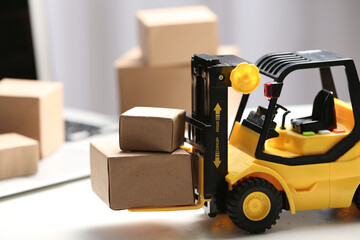 Toy forklift with boxes near laptop on table. Logistics and wholesale concept