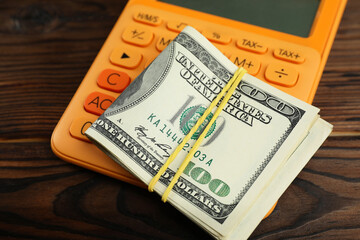 Money exchange. Dollar banknotes and calculator on wooden background, closeup
