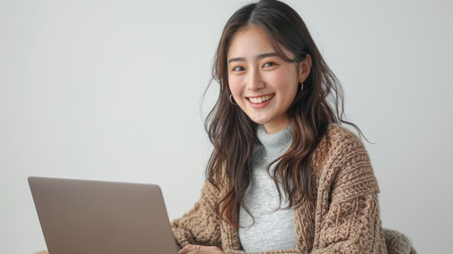 A cheerful young woman sits in front of a laptop, her gaze directed towards the camera, pleasant smile
