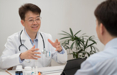 Obraz premium A middle-aged Asian male doctor and a male patient undergoing counseling at a hospital