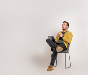 Male entrepreneur with laptop thinking business ideas and sitting on chair over white background