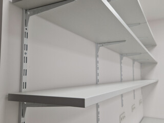 empty white room with gray carpet and shelves along entire wall. metal holders and laminate shelves...