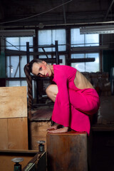 A young woman in a pink knitted dress poses in an abandoned industrial building.