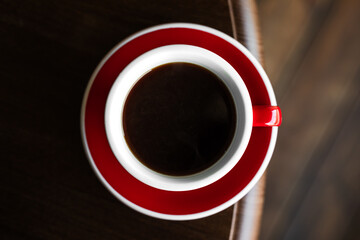 Top view of a red cup of black coffee on a saucer on the edge of wooden table, copy space