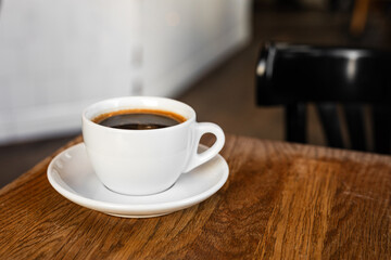 A white cup of black coffee on a saucer on the wooden table in a cafe - 744463341