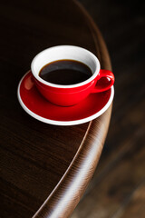 A red cup of black coffee on a saucer on the edge of wooden table, copy space - 744463531
