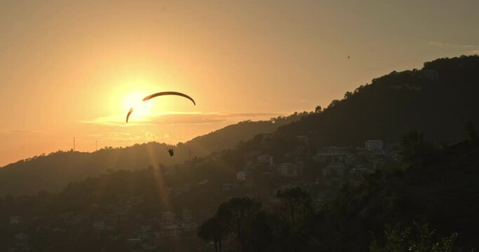 A mesmerizing silhouette emerges as a paraglider gracefully crosses the backdrop of the setting sun in Dharamshala, Himachal Pradesh, painting the sky with a stunning blend of colors and adventure.