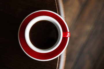 Top view of a red cup of black coffee on a saucer on the edge of wooden table, copy space - 744463774