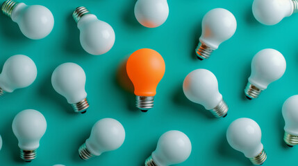 An orange lightbulb glowing among a group of white lightbulbs on a teal background, representing a unique idea or solution.
