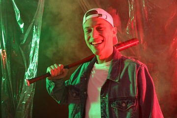 Fototapeta premium Young man with baseball bat on color background in neon lights