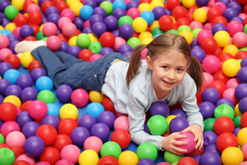 Fototapeta na wymiar Happy little girl lying on many colorful balls in ball pit