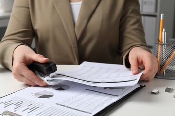 Woman stapling documents at white table indoors, closeup