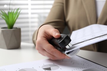Woman with documents using stapler at white table indoors, closeup
