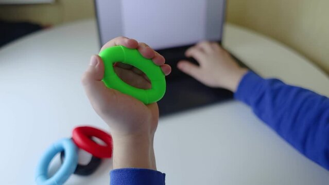 Hand gripper. Man squeezes rubber expander while working on his laptop. Concept of combining useful activity with necessary work. Training hand and arm muscles. Multi-colored mini training apparatus