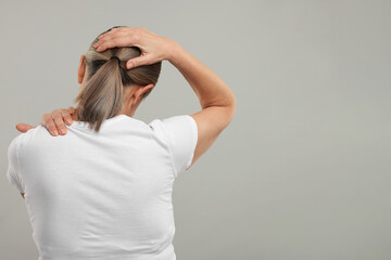 Mature woman suffering from pain in her neck on grey background, back view. Space for text