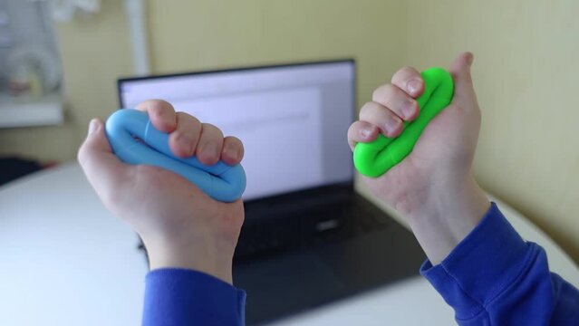 Hand gripper. Man squeezes rubber expander while working on his laptop. Concept of combining useful activity with necessary work. Training hand and arm muscles. Multi-colored mini training apparatus