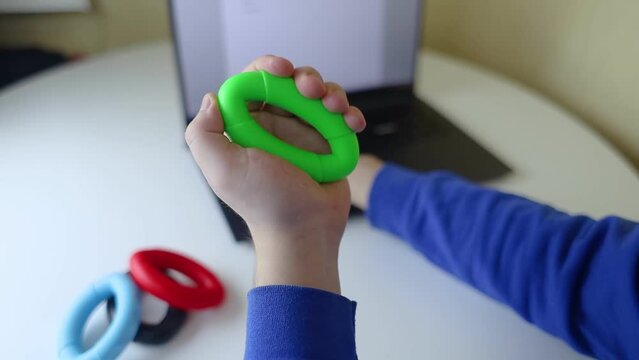 Hand gripper. Man squeezes rubber expander while working on his laptop. Concept of combining useful activity with necessary work. Training hand and arm muscles. Multi-colored mini training apparatus