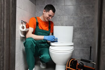 Smiling plumber repairing toilet bowl in water closet