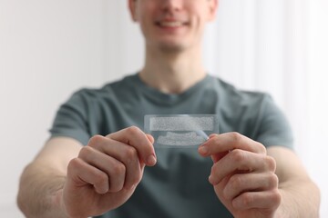 Young man with whitening strips on light background, closeup
