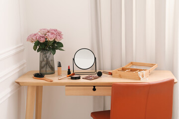 Mirror, cosmetic products, box of jewelry and vase with pink roses on wooden dressing table in makeup room