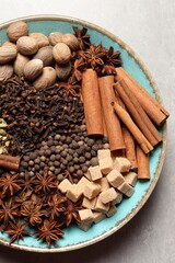 Different spices and nuts in bowl on light gray textured table, top view