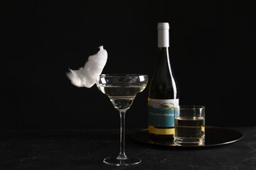 Cocktail with tasty cotton candy and bottle of alcohol drink on dark textured table against black background
