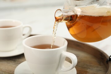 Pouring aromatic tea in cup at table, closeup