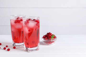 Tasty cranberry juice with ice cubes in glasses and fresh berries on white wooden table. Space for text