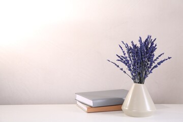 Bouquet of beautiful preserved lavender flowers and notebooks on white table near beige wall, space for text